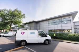 A-white-van-is-parked-outside-a-large-building,-indicating-a-cleaning-service-presence.