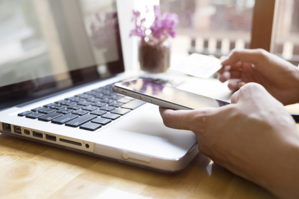 Person-holding-a-smartphone-and-credit-card-next-to-a-laptop,-representing-the-mobile-online-shopping-and-checkout-experience