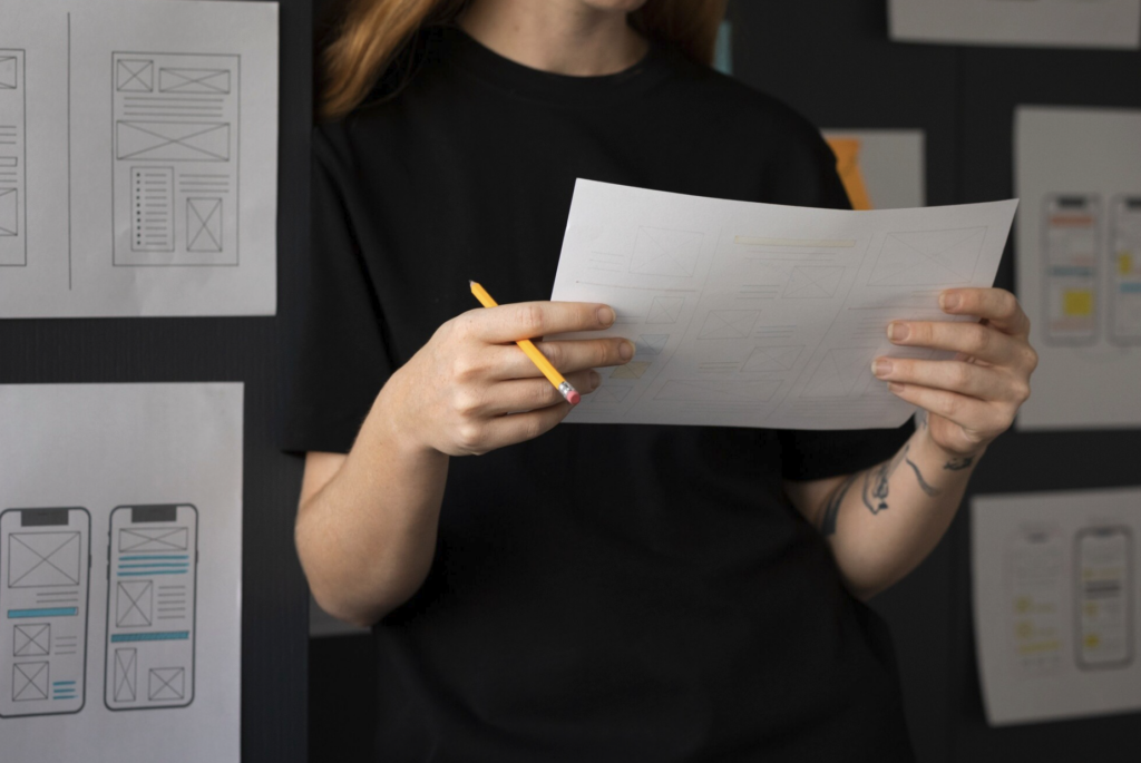 Woman-with-pencil-reviewing-wireframe-sketch-amid-UI-mockups.