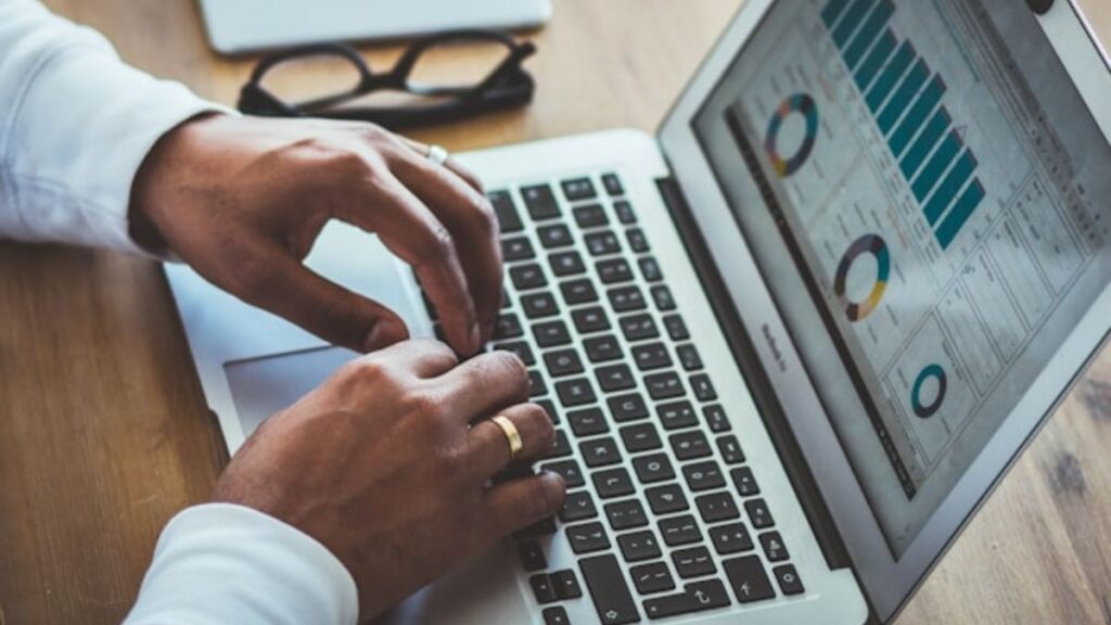 Hands typing on a laptop with a data dashboard on screen